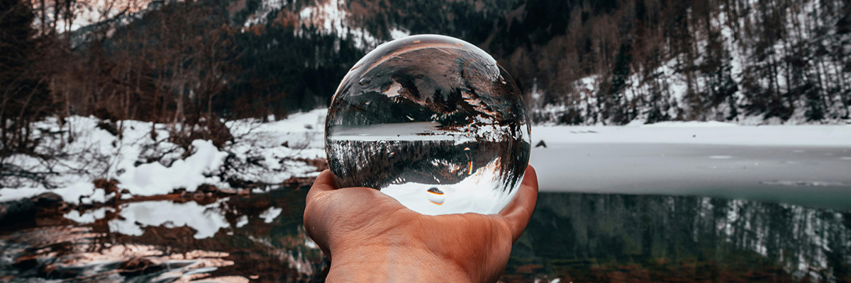 A crystal ball on a snow bank reflects an upside down forest scene in the winter.