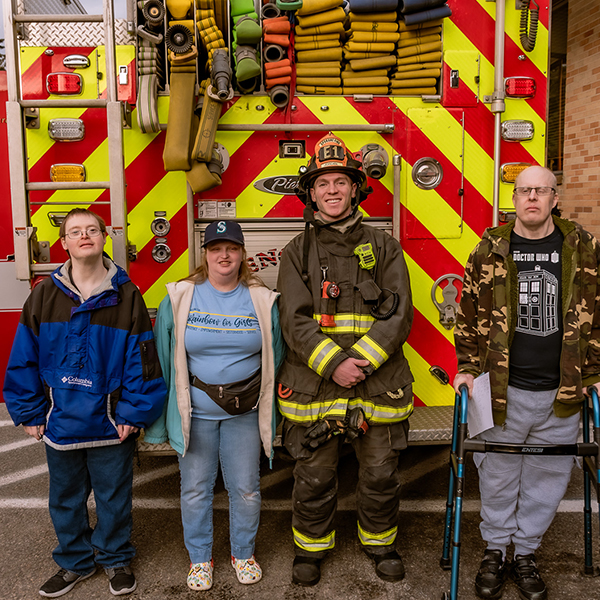 Members of the Community Center stand for a photo op with a firefighter in front of a red and yellow fire engine.